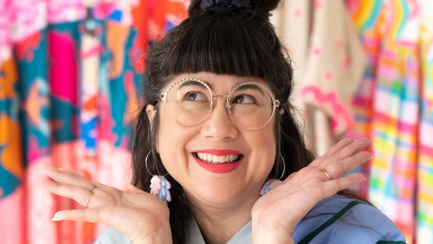 Sue-Ching Lascelles smiling with her hands up and wearing colourful clothing