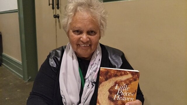 An older woman sitting down and holding a book to the camera