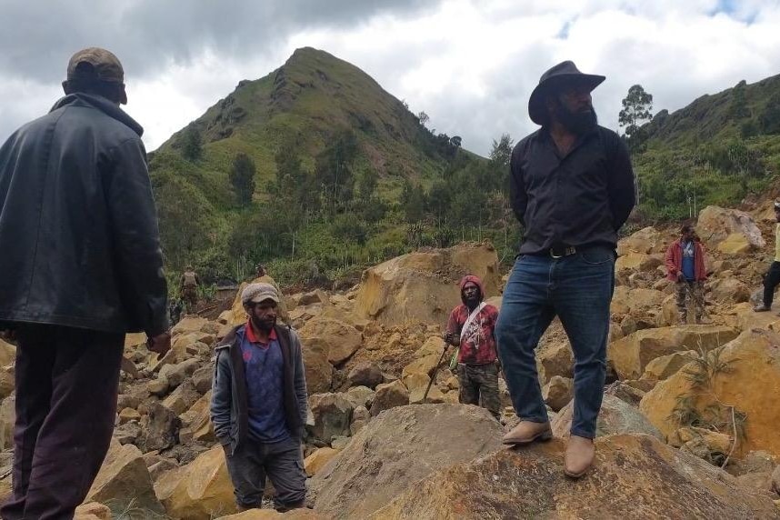 A group of men stand on rocks after a landslide on a mountain.