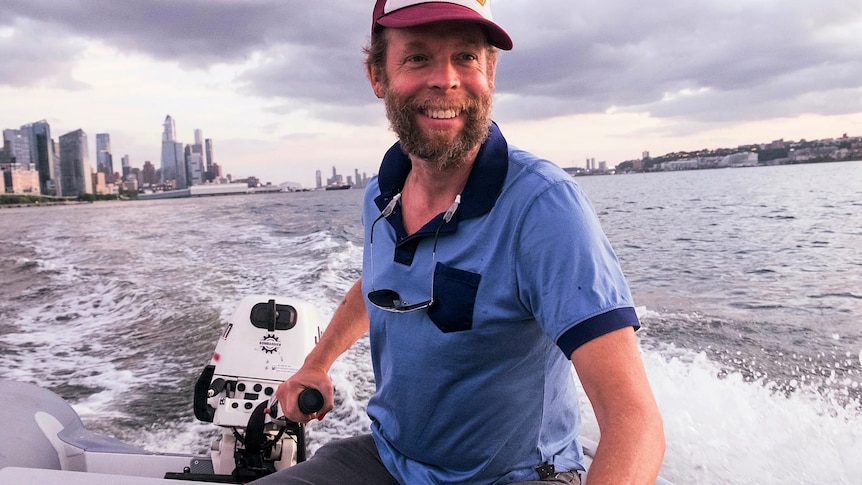 Musician Will Oldham in a boat on a large river with a smile on his face
