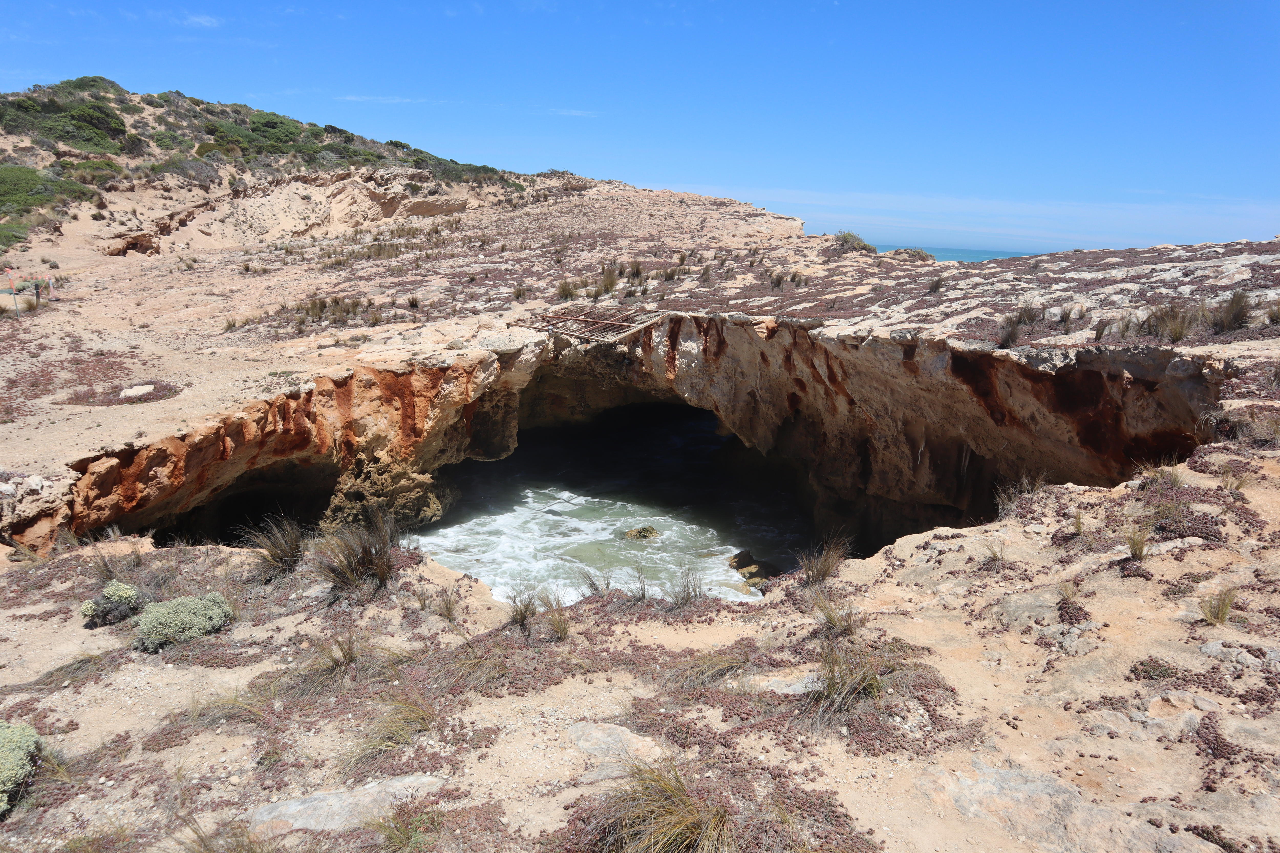 A limestone cliff with a large hole down to water below.