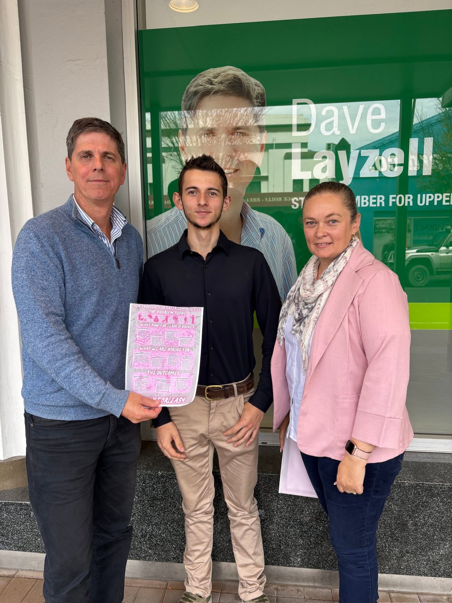 Dave Layzell stands next to a woman and a teenage boy holding a pink information sheet, outside his Singleton office