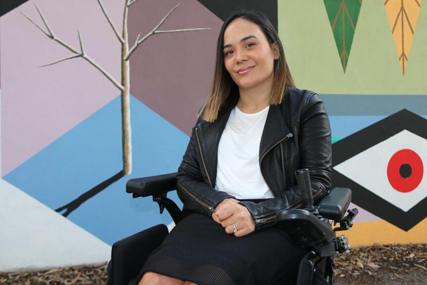 Jocelyn Franciscus poses for a picture in her wheelchair in front of a wall featuring artwork.