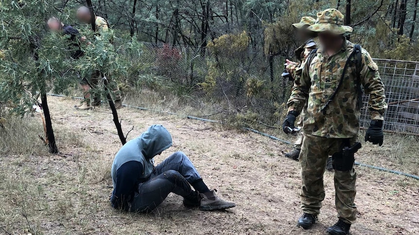 Four officers wearing camouflage with a man handcuffed on the ground.