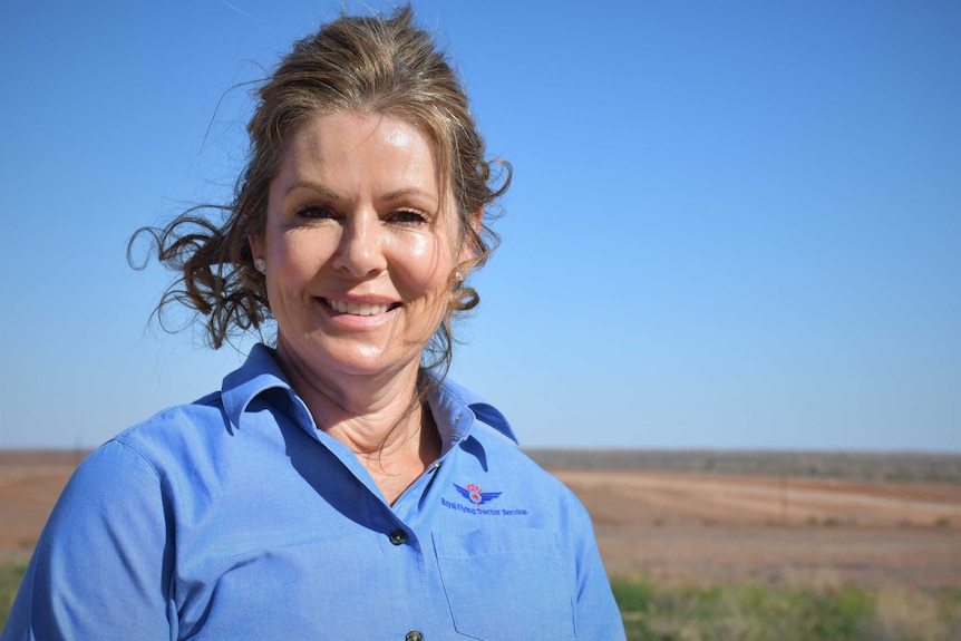 A lady with blonde hair and a blue shirt smiles and looks at the camera