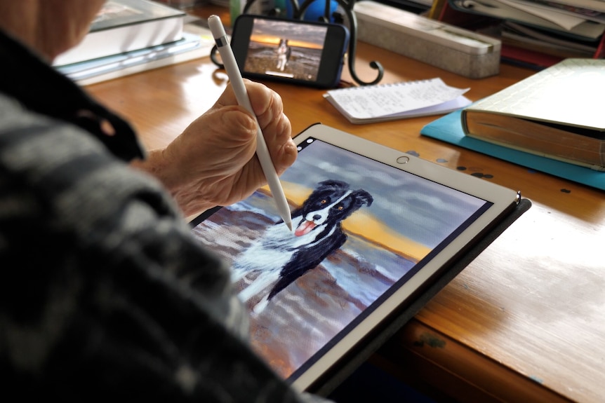 A woman holding a digital pencil draws painting of a dog on a digital tablet.