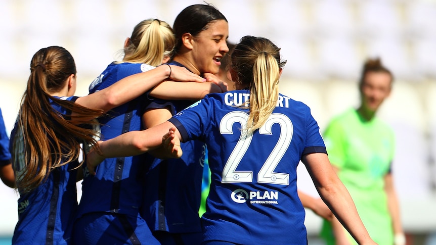 A group of female footballers throw their arms around a striker who has just scored a goal.