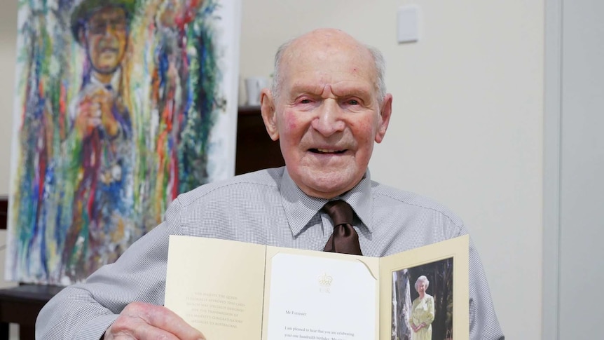 Arnold looks front on smiling holding a letter from the Queen wearing a brown tie