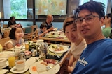 An Asian family with two young parents with two school-age children smile at camera from a table in restaurant