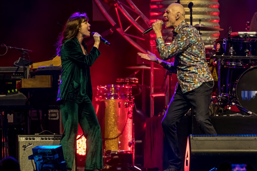 A woman wearing black with brunette hair singing with a bald man with a patterned shirt