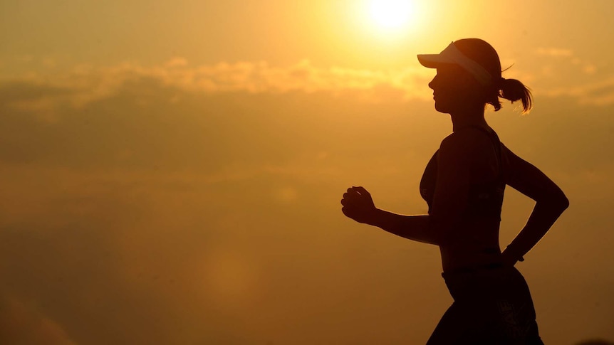 A woman in a cap runs with the sun in the background.