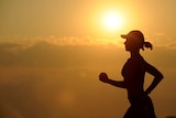 A woman in a cap runs with the sun in the background.