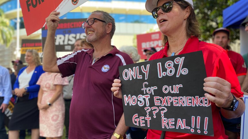 Two people protesting in the Darwin CBD, one of whom is holding a sign saying 'Only 1.8% for our most experienced? Get real'.