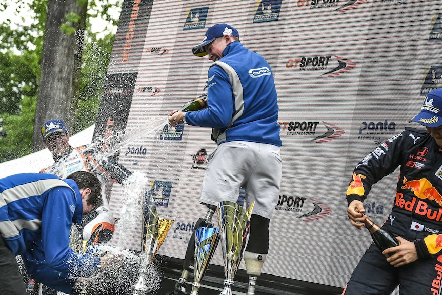 Billy Monger stands on the podium, spraying champagne at his teammates
