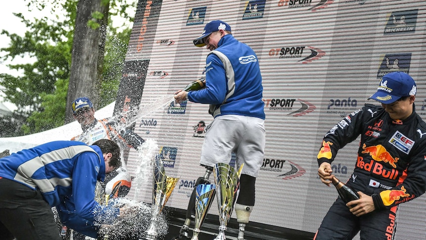 Billy Monger stands on the podium, spraying champagne at his teammates