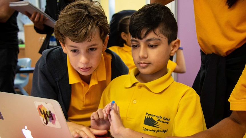 Two young boy students from Reservoir East Primary School learn financial literacy on a laptop.