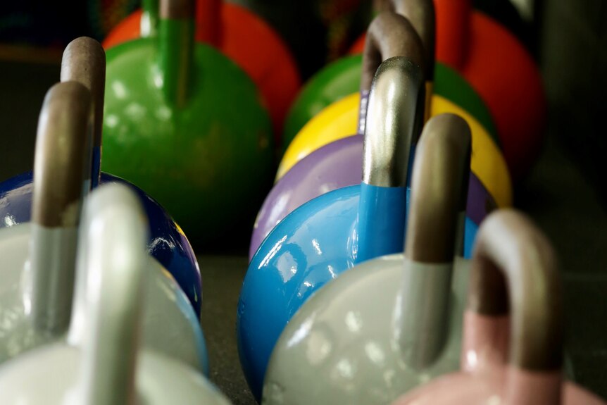 Colourful kettlebells are lined up on the floor of a gym.