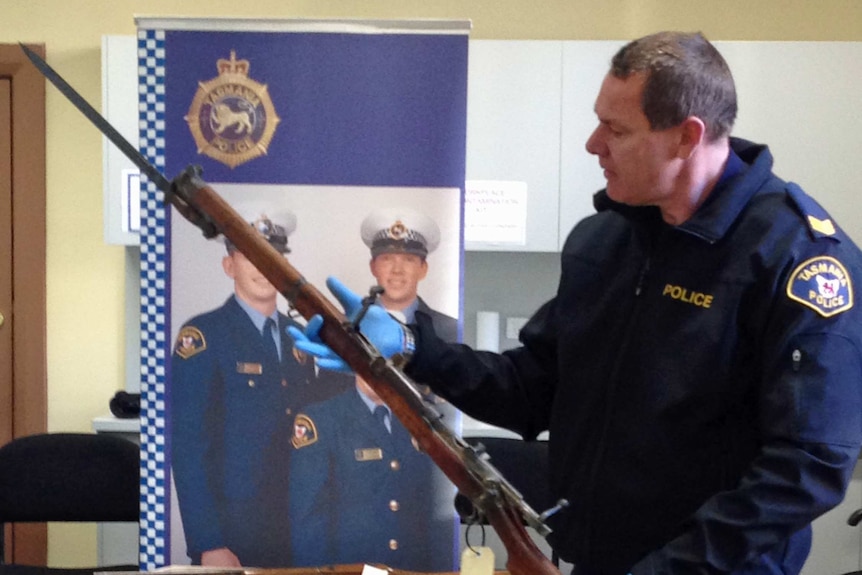 A police officer examines a rifle handed in during the Tasmanian firearm amnesty