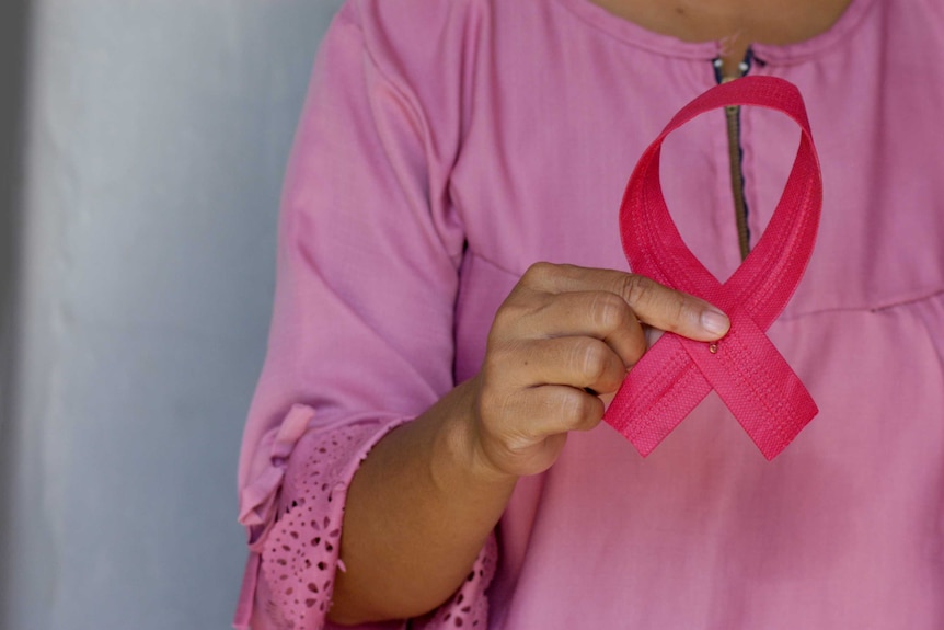 Woman in pink shirt holds up pink ribbon signifying breast cancer awareness.