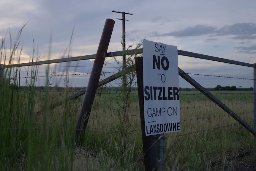 A sign on a barbed wire fence reads "SAY NO TO SITZLER CAMP ON LANSDOWNE"