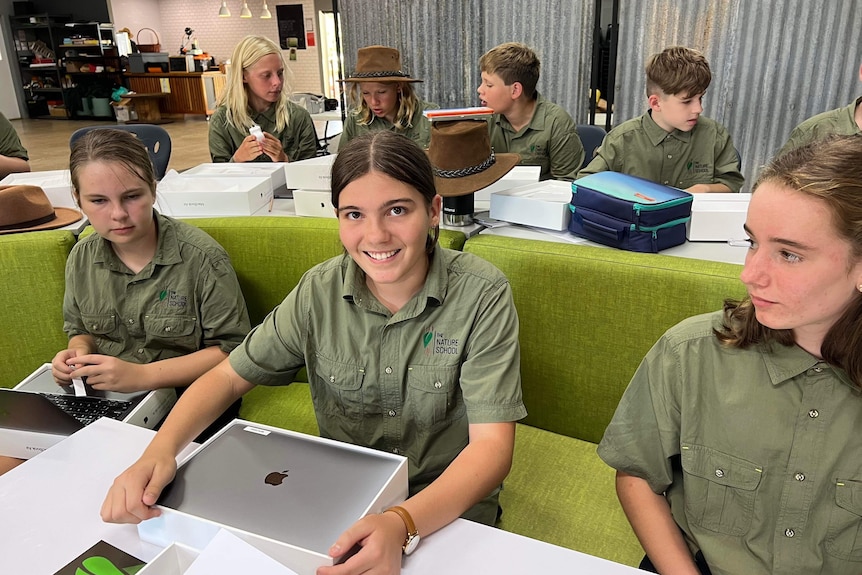 Year 7 students in green shirts sit at desks looking at new laptops.