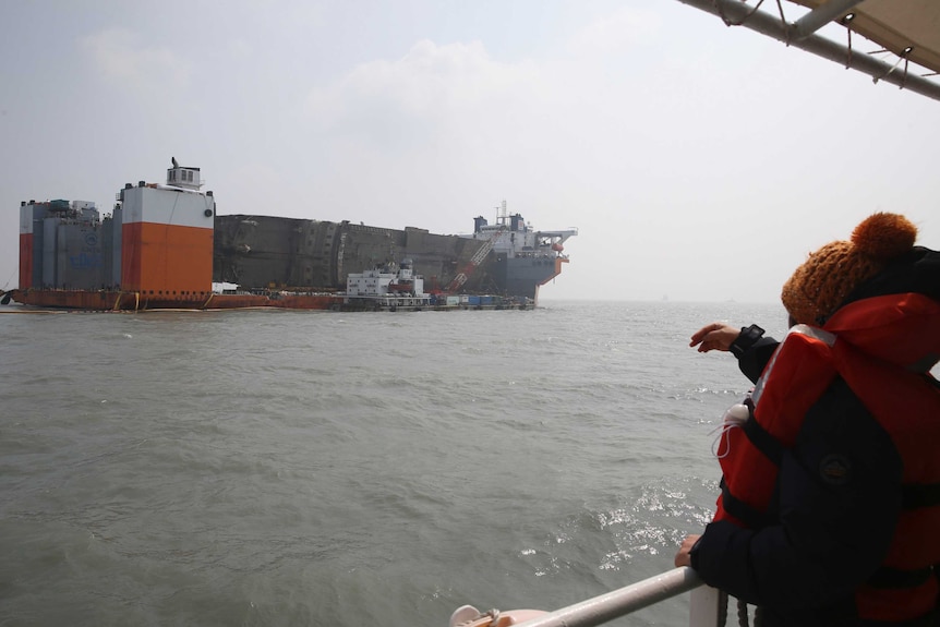 A person looks on as a salvaged ferry is transported back to land