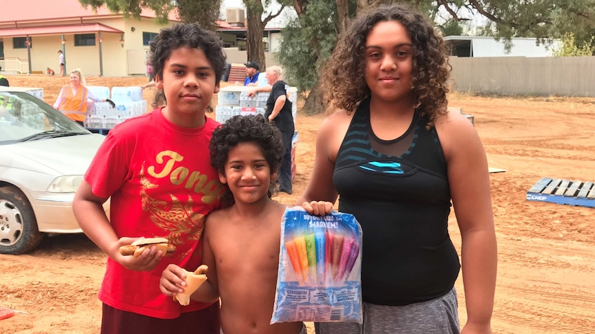 Three children holding a packet of ice blocks and sausages in bread.