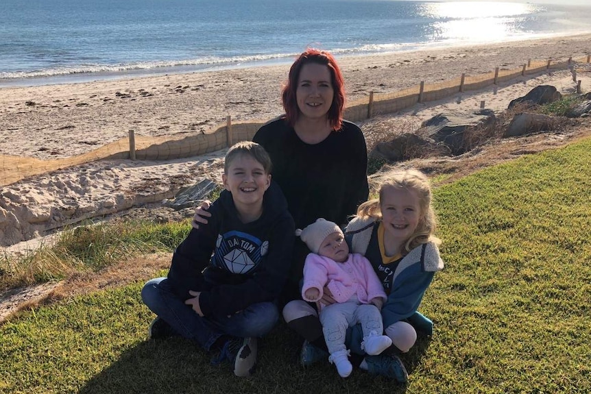 Samantha Richardson sits on a beach foreshore with her three children.