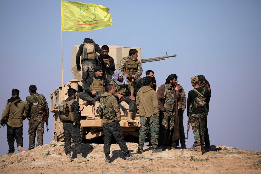 A group of Syrian Democratic Forces fighters cluster around a tank with a flag flying.
