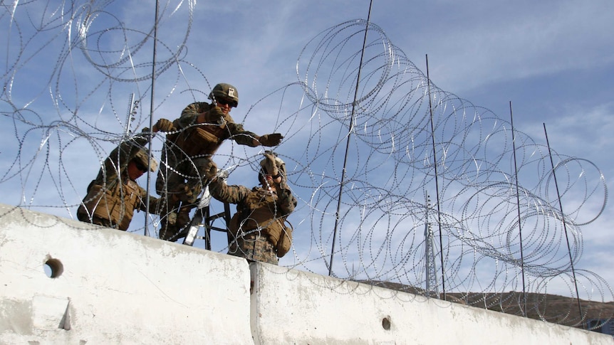 Two Marines hold another as he erects a barbed-wire fence above a concrete barricade.