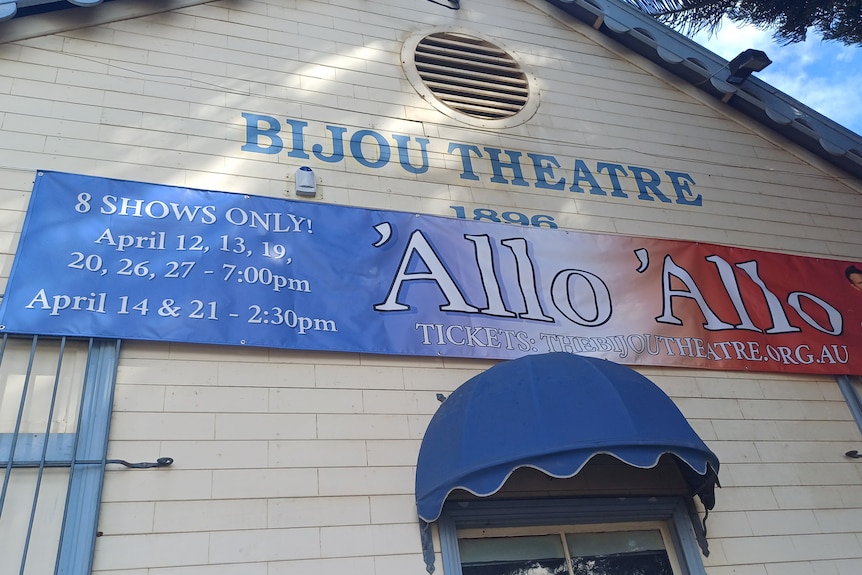 L'extérieur d'un théâtre local peint en blanc et bleu pâle, avec une pancarte indiquant Théâtre Bijou. 