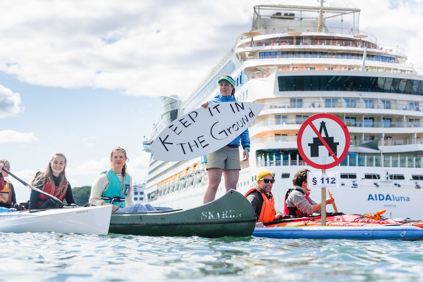 People on canoes on water in front of a cruise ship