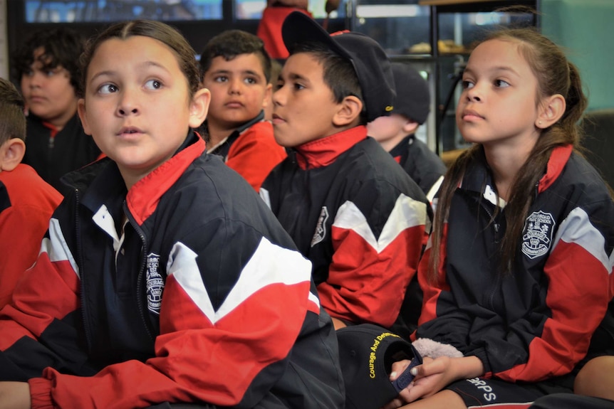 A group of young children sit on the floor during class.