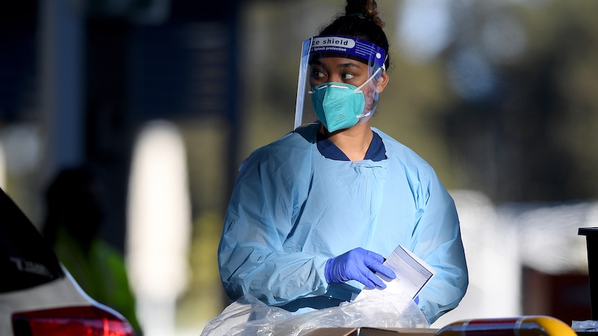 Dark-haired female health worker in blue coveralls and face shield