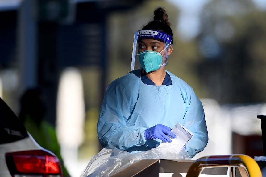 Dark-haired female health worker in blue coveralls and face shield