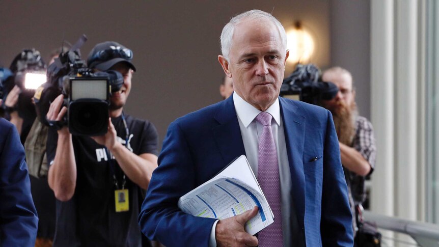 Prime Minister Malcolm Turnbull purses his lips as he is followed by cameramen through Parliament House