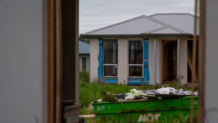 A house under construction with a green skip bin in the foreground