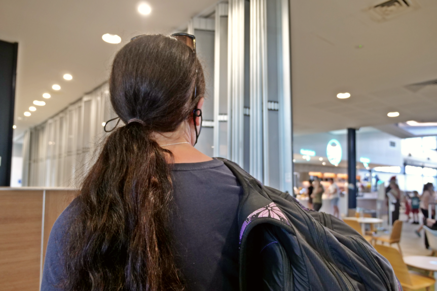 a woman with a backpack looks towards a crowded airport lounge