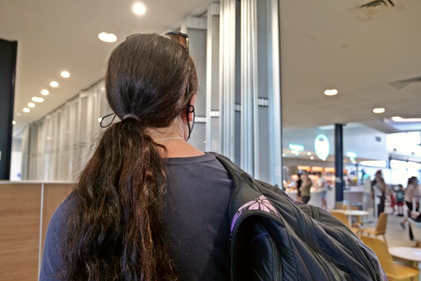 a woman with a backpack looks towards a crowded airport lounge