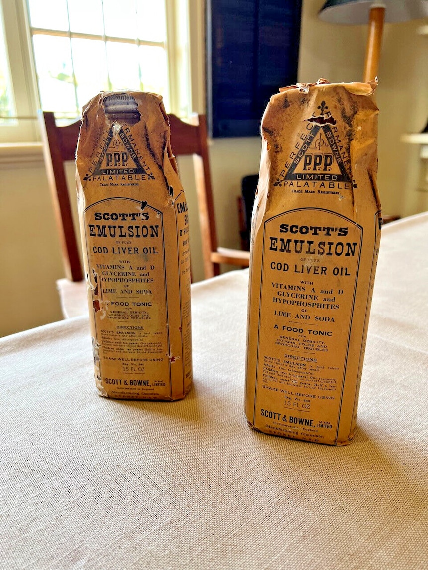 Two vintage bottles of Scott's Emulsion sit on a table. The bottles are covered in paper wrapping.