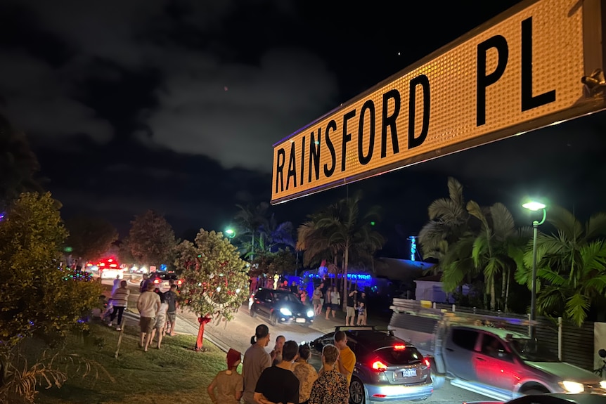 Street sign at night with people behind in groups