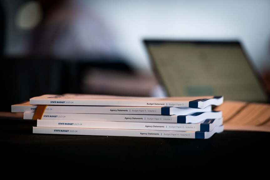 A stack of white books with a blurred laptop screen in the background