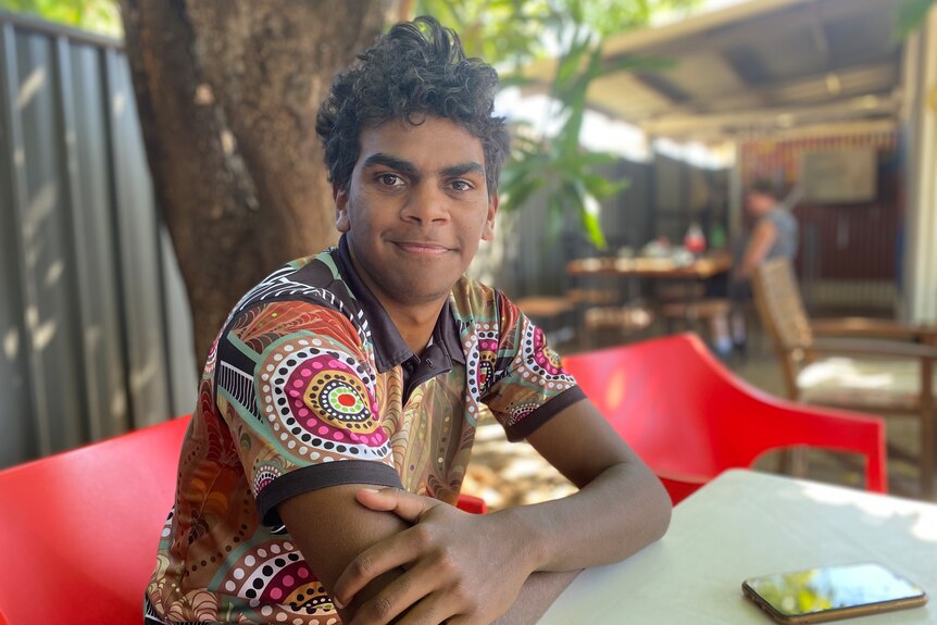 A smiling young man with an indigenous print shirt on 