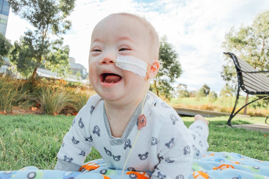 Baby Leo Yang smiles while lying on a blanket outside.