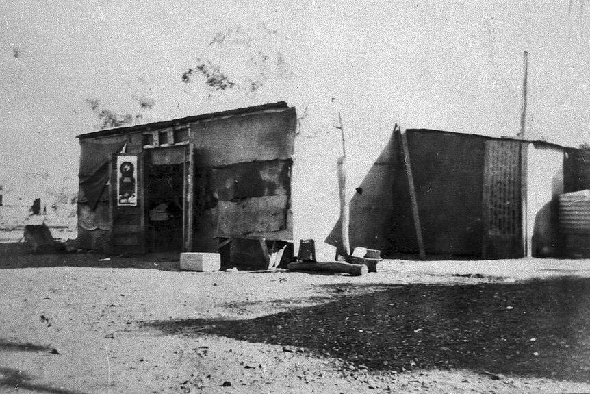 An old black and white image of a small shack with open door.