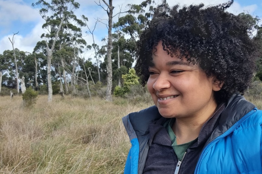 Woman looking to her right and smiling, in a bushland setting.