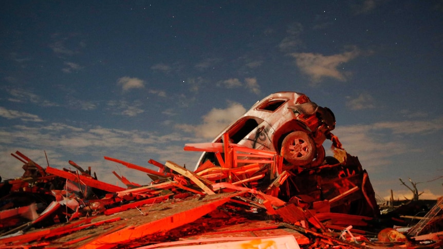 A vehicle sits on a pile of debris from the destruction caused by a tornado in Illinois.