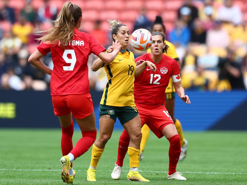 Women soccer players, some dressed in red while another is in yellow and green, during a match