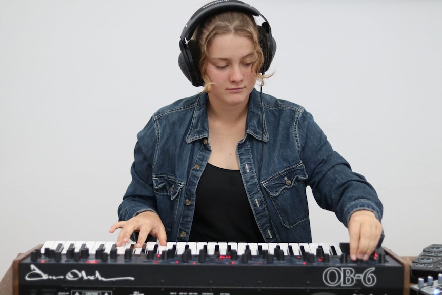 A young woman plays a keyboard-type instrument and wears headphones.