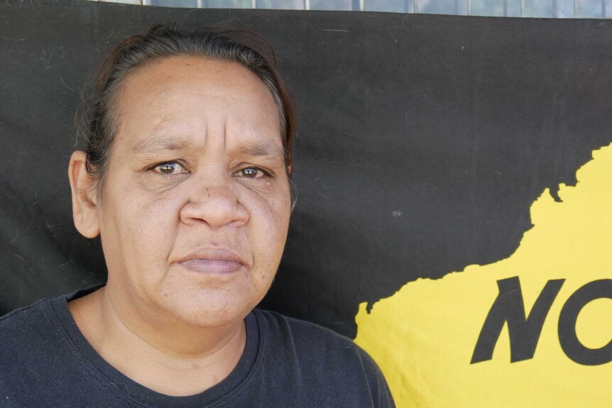 A portrait photo of Barb Shaw, an Indigenous woman from Alice Springs, she is standing in from of an indigenous protest banner.